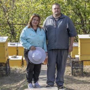 Ukrainian woman and man stand among bee hives.