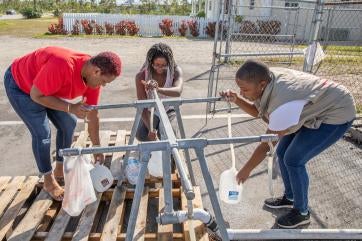 Three prosper global colleagues fill up water from spigots.