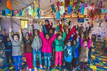 Group of child refugees smiling with their arms raised at a prosper global youth center surrounded by bright decorations