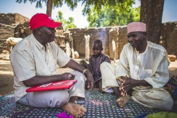 A prosper global employee, left, talking with alhaj, who is with a young boy.