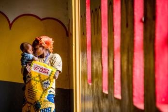 A woman holding her son in front of a yellow mural