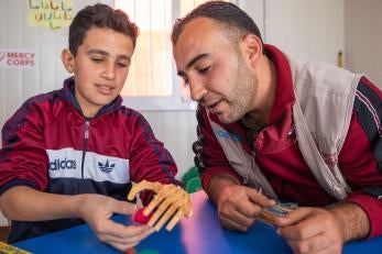 A young person works with prosper global shadow teacher saleh alshalabi, learning how to strengthen his muscles and use his new prosthetic hand.