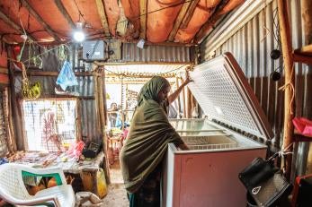 A shop owner accessing products in a refrigerator inside their store.