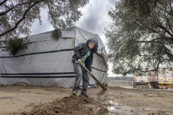 A young boy digs a trench around his tent to keep water away