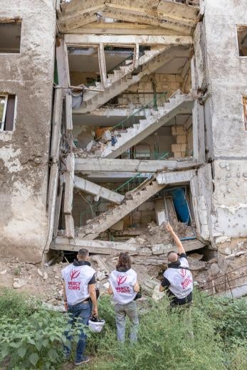 Prosper global humanitarian workers in front of a damaged residential building