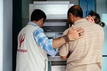 Prosper Global team member helping a father (holding his daughter) to use an ATM