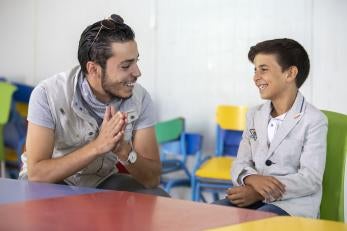 At a youth center in Zaatari, Omar Al-Tal sits with Mohammad. Mohammad is able to play sports and games while learning important life skills like computers and English. Two of Mohammad’s favorite activities are playing foosball and soccer, but his favorite is singing. At a recent talent show in the center, he finished third. Photo: Ezra Millstein/Prosper Global