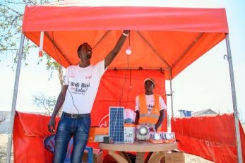 A person hangs a light in a temporary pop-up canopy filled with solar electrical equipment. 