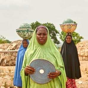 Three nigerian woman in traditional dress; two with balanced loads on their heads.