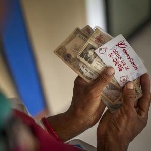 Image: hands holding cash and a prosper global id card during a distribution of emergency cash