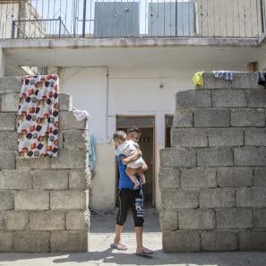 A boy in a cinderblock doorway holding a baby
