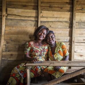 A mother and daughter sit together on a wood bench.