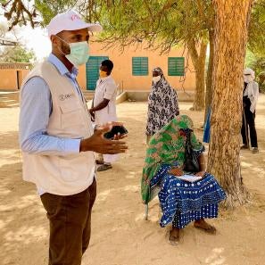 Participants in tillaberi region, niger, listen to a prosper global representative wearing a facemask explaining details about a program.