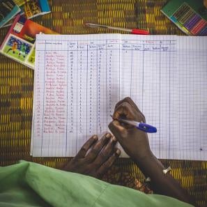 A hand holding a pen marks a paper spreadsheet.