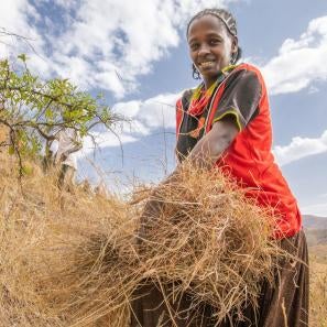 An adult smiles for the camera while cutting grass on a hill in ethiopia.