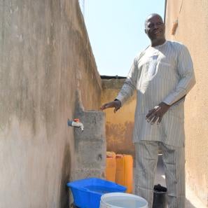 A person standing next to a tap in their compound connected to the local water facility.