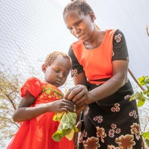 A mother teaching her daughter to pick vegetables from their garden.