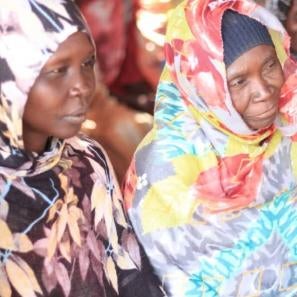 Two people sitting together listening to someone speak at a gathering..