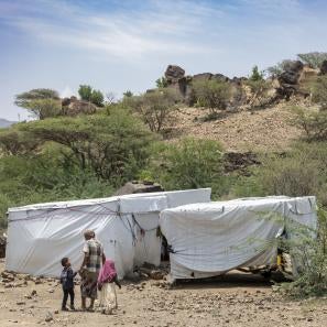 Family stands in front of makeshift shelters in yemen.