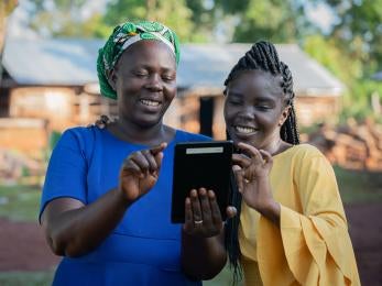 Two women consulting a tablet device and smiling.
