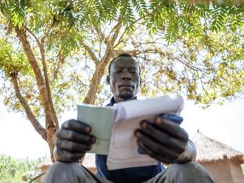 Ugandan man sits under a tree reviewing notes.